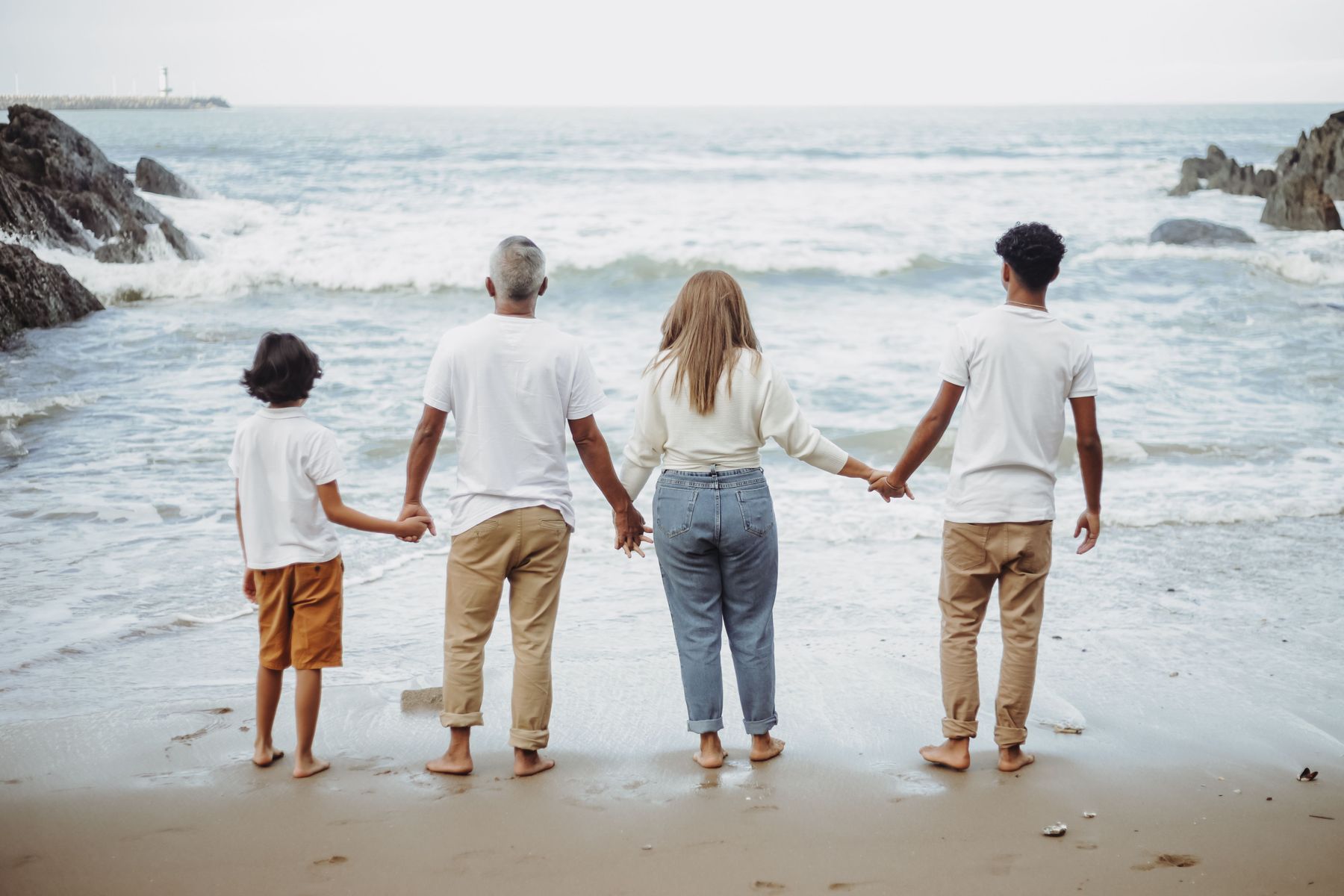 A family holding hands at the beach, facing the ocean